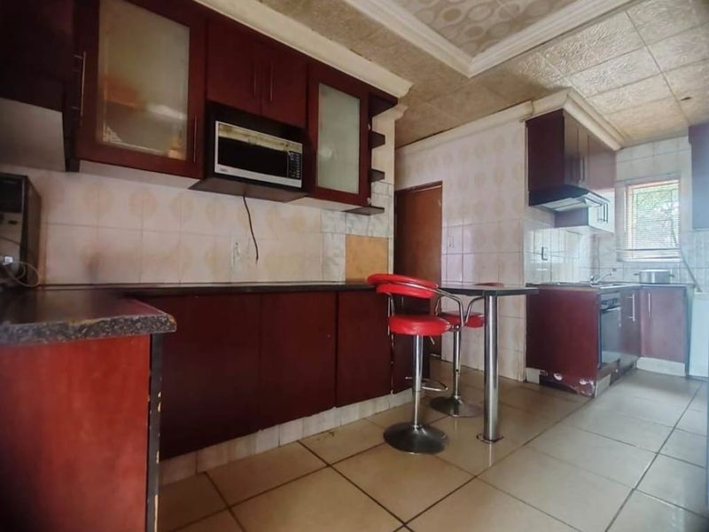 A dated kitchen featuring dark wood cabinetry, tiled backsplash, and tiled flooring, offering potential for a modern renovation.
