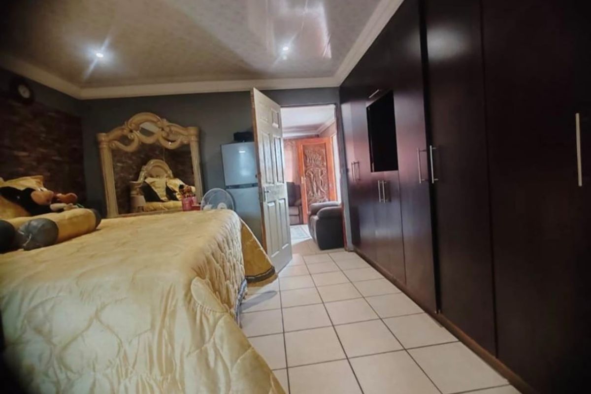 Spacious bedroom featuring large built-in dark wood cupboards, tiled flooring, and recessed ceiling lighting, offering ample storage and a functional layout.