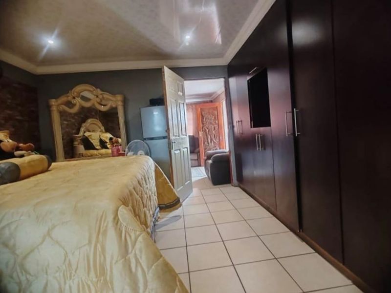 Spacious bedroom featuring large built-in dark wood cupboards, tiled flooring, and recessed ceiling lighting, offering ample storage and a functional layout.