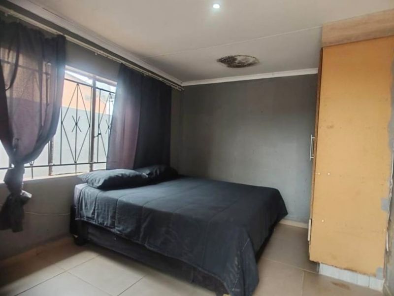 A bedroom featuring tiled flooring, a built-in wardrobe, and security bars on the window, showing signs of ceiling water damage and general wear.