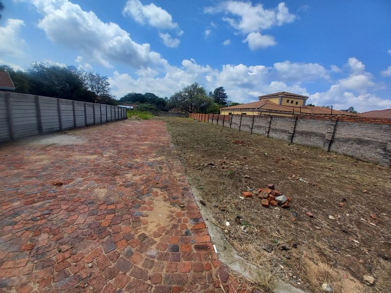 A vacant residential plot featuring a cobblestone paved driveway area, enclosed by precast concrete and brick boundary walls.