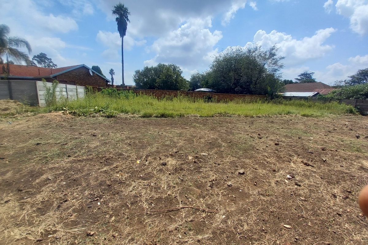 A vacant residential plot featuring a mix of cleared earth and overgrown vegetation, enclosed by precast concrete and brick boundary walls.
