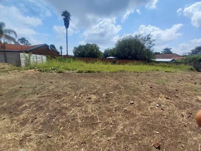 A vacant residential plot featuring a mix of cleared earth and overgrown vegetation, enclosed by precast concrete and brick boundary walls.