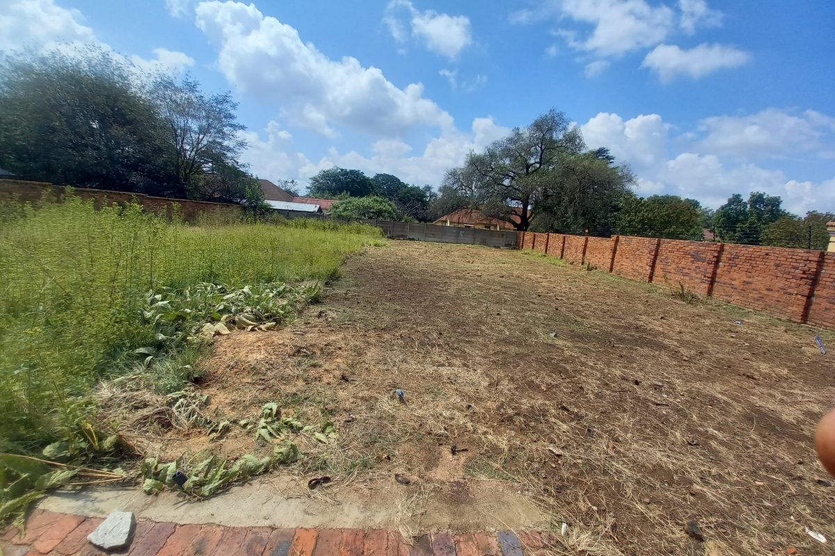 A vacant residential plot featuring a brick boundary wall and natural ground cover, suitable for future development.
