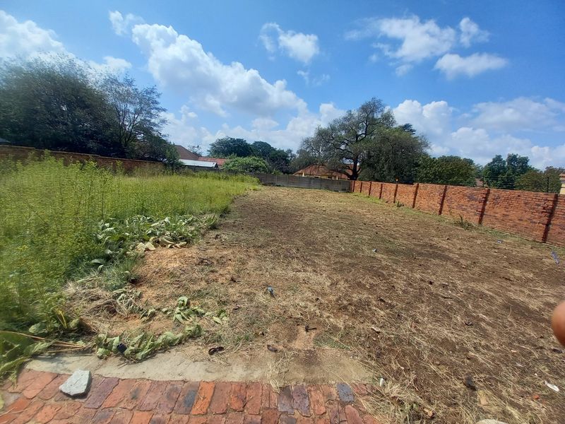 A vacant residential plot featuring a brick boundary wall and natural ground cover, suitable for future development.