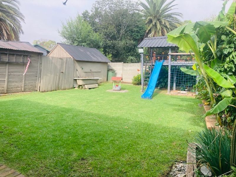 A spacious backyard featuring a well-maintained lawn, a timber storage shed, and a built-in children's play structure with a slide.