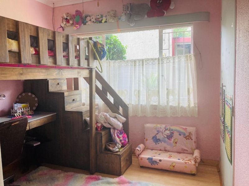 A bedroom featuring a built-in wardrobe and window security bars, currently styled as a child's room with pink walls and light-toned flooring.
