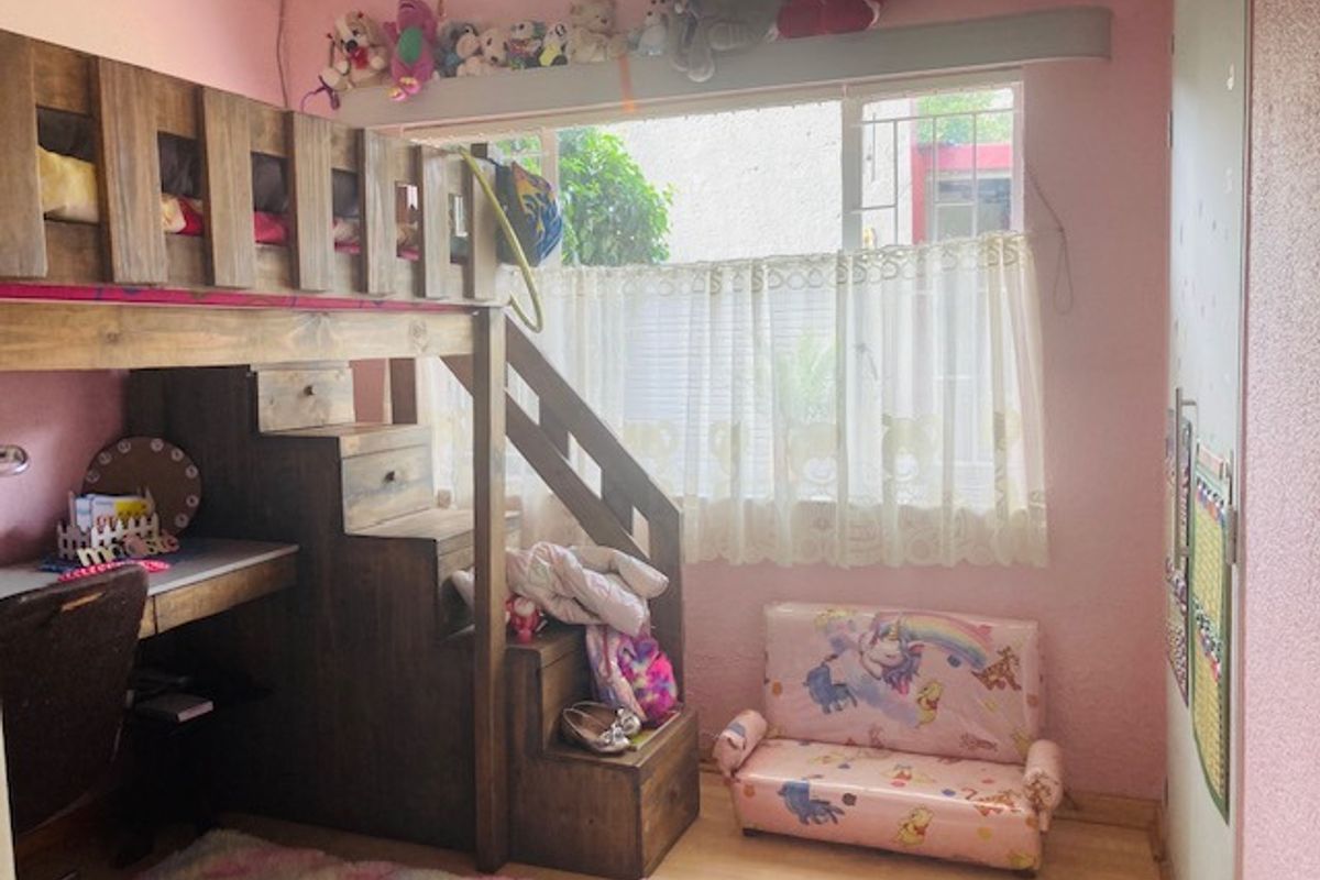 A bedroom featuring a built-in wardrobe and window security bars, currently styled as a child's room with pink walls and light-toned flooring.