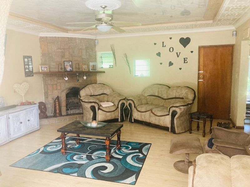 A living room featuring a stone fireplace, laminate flooring, and a ceiling fan, offering a cozy and traditional atmosphere.