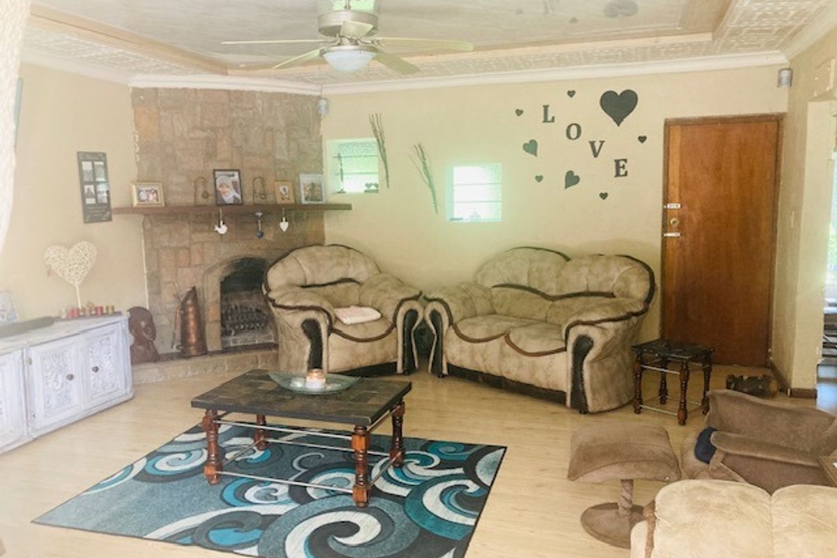 A living room featuring a stone fireplace, laminate flooring, and a ceiling fan, offering a cozy and traditional atmosphere.
