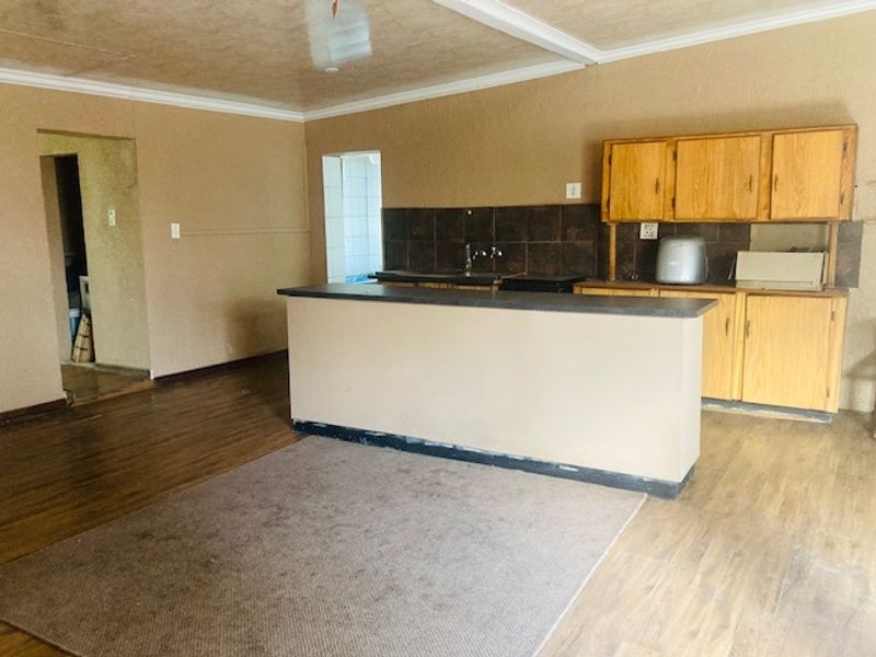 Open plan kitchen area featuring a central island, wooden cabinetry, and tiled backsplash, offering a functional layout ready for modernization.