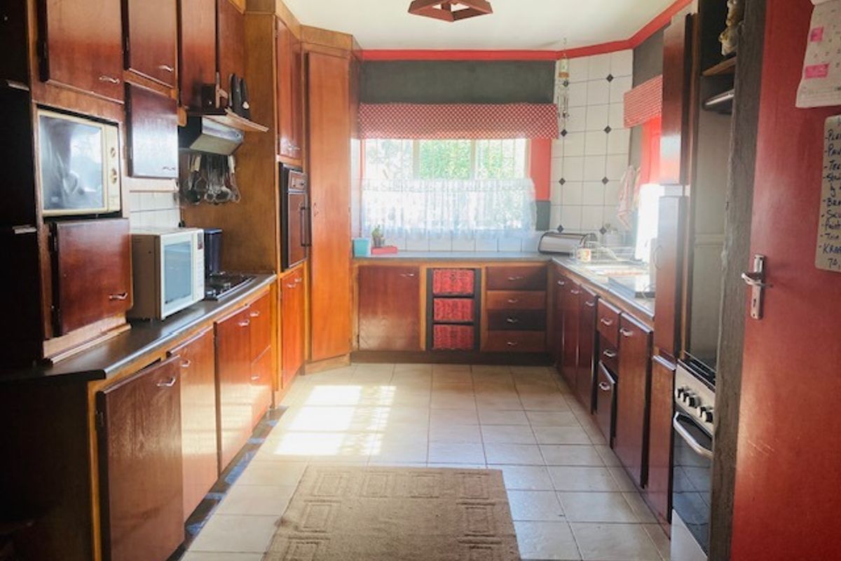 A dated kitchen featuring extensive wooden cabinetry, tiled flooring, and built-in cooking appliances, offering significant potential for a modern renovation.
