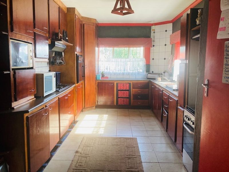 A dated kitchen featuring extensive wooden cabinetry, tiled flooring, and built-in cooking appliances, offering significant potential for a modern renovation.