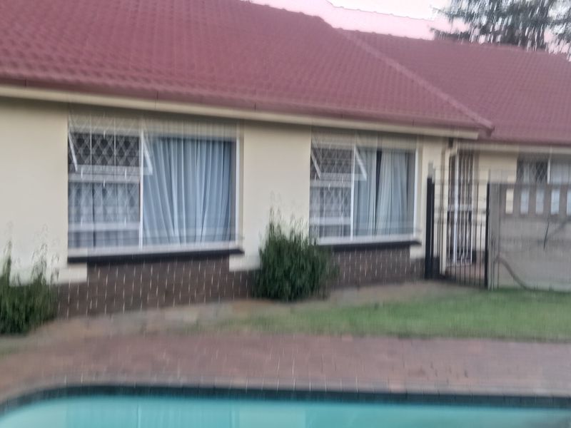 Rear view of the house featuring a swimming pool, brick boundary wall, and tiled roof structure.