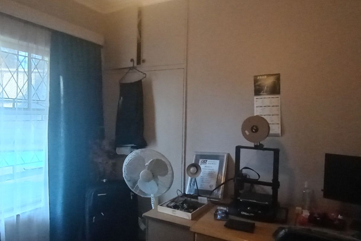 A bedroom featuring a built-in cupboard and a window fitted with security bars, currently utilized as a workspace.