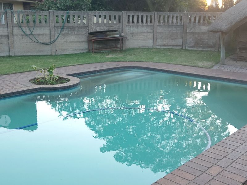 Outdoor pool area featuring a swimming pool with brick paving, a thatch lapa, and a precast concrete boundary wall.