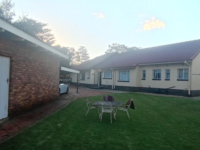 A view of the rear exterior of the house featuring a brick outbuilding, a paved path, and a spacious lawn area.