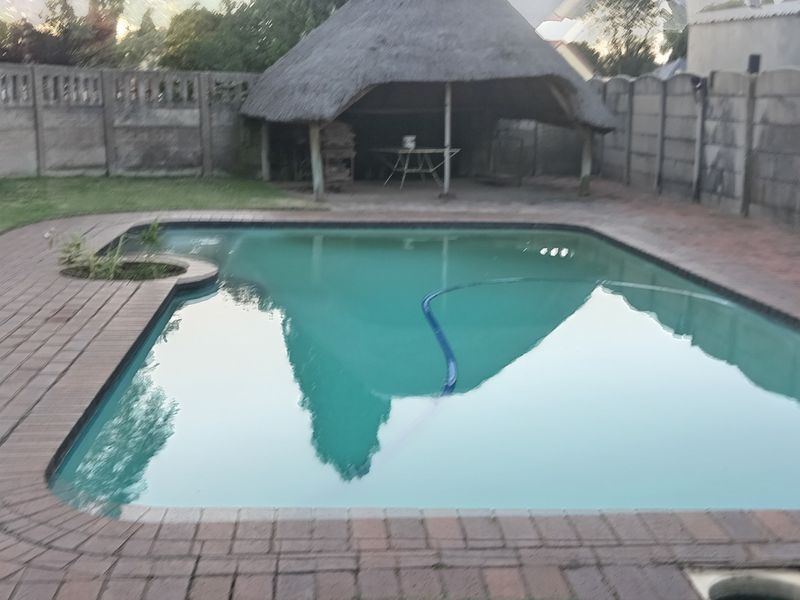 Outdoor pool area featuring a swimming pool, brick paving, and a traditional thatched lapa, enclosed by precast concrete boundary walls.