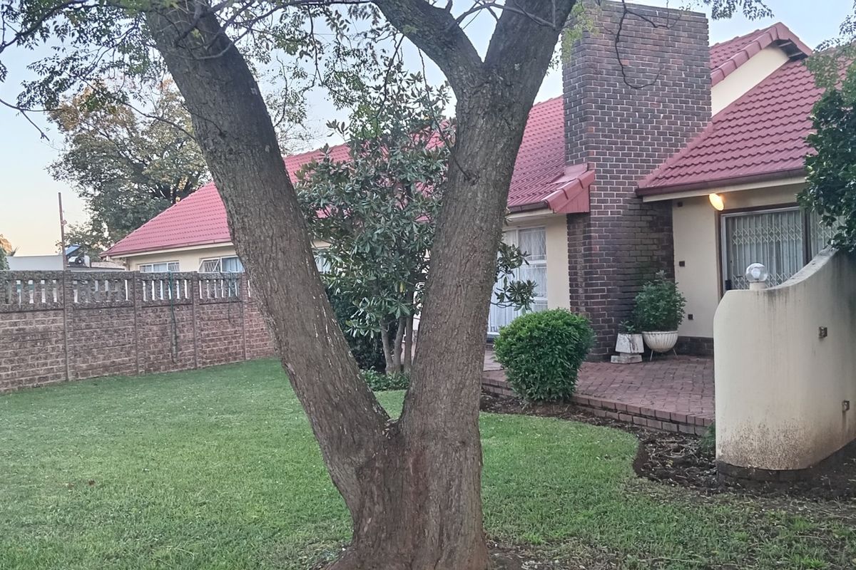 Rear garden view featuring a paved patio area, brick chimney stack, and established lawn enclosed by a brick boundary wall.