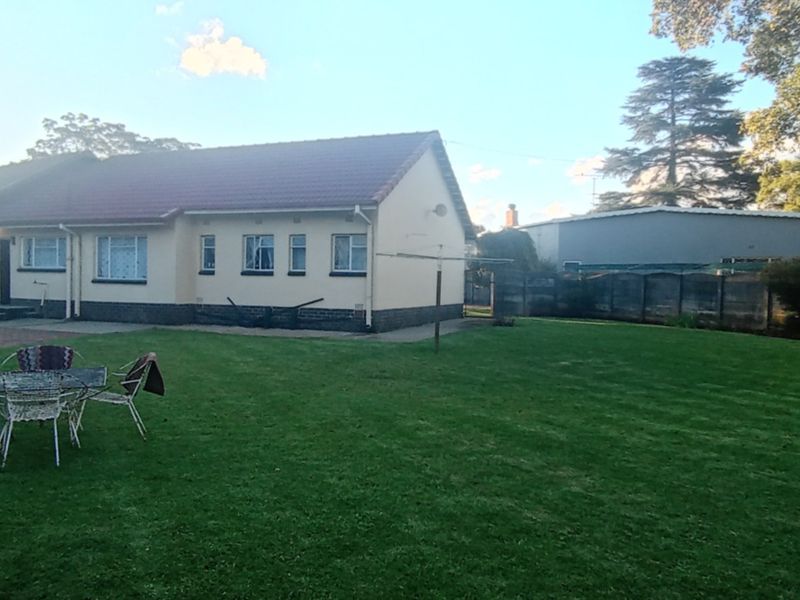 A view of the rear exterior of the house featuring a large lawn, paved driveway area, and perimeter boundary walling.