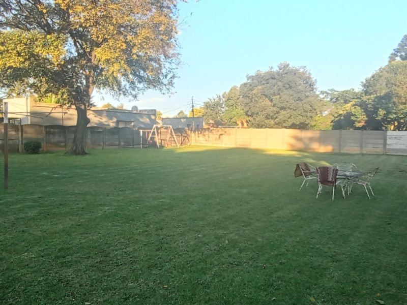 A spacious, well-maintained backyard featuring a large lawn, mature trees, and secure precast concrete boundary walling.