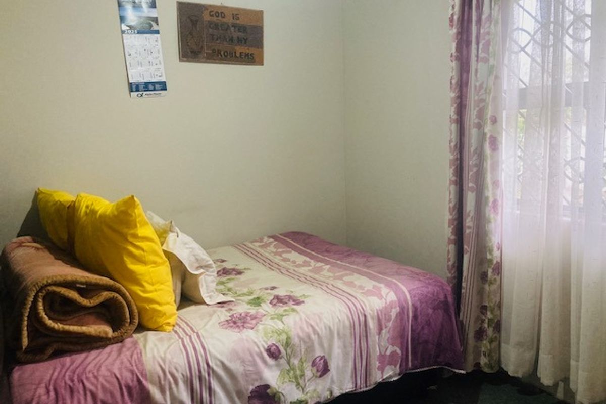 A standard bedroom featuring a window with a security gate and curtain rod, providing natural light and basic security.