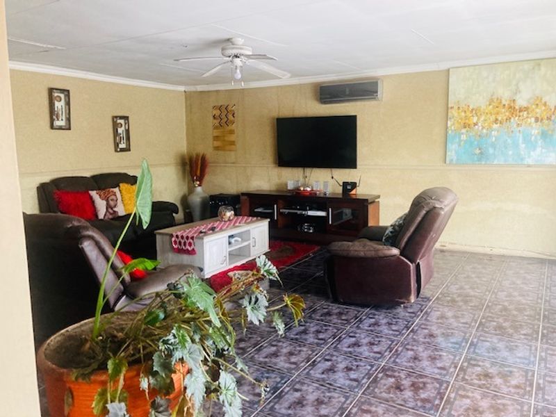 Spacious living room featuring tiled flooring, a ceiling fan, and a wall-mounted air conditioning unit.