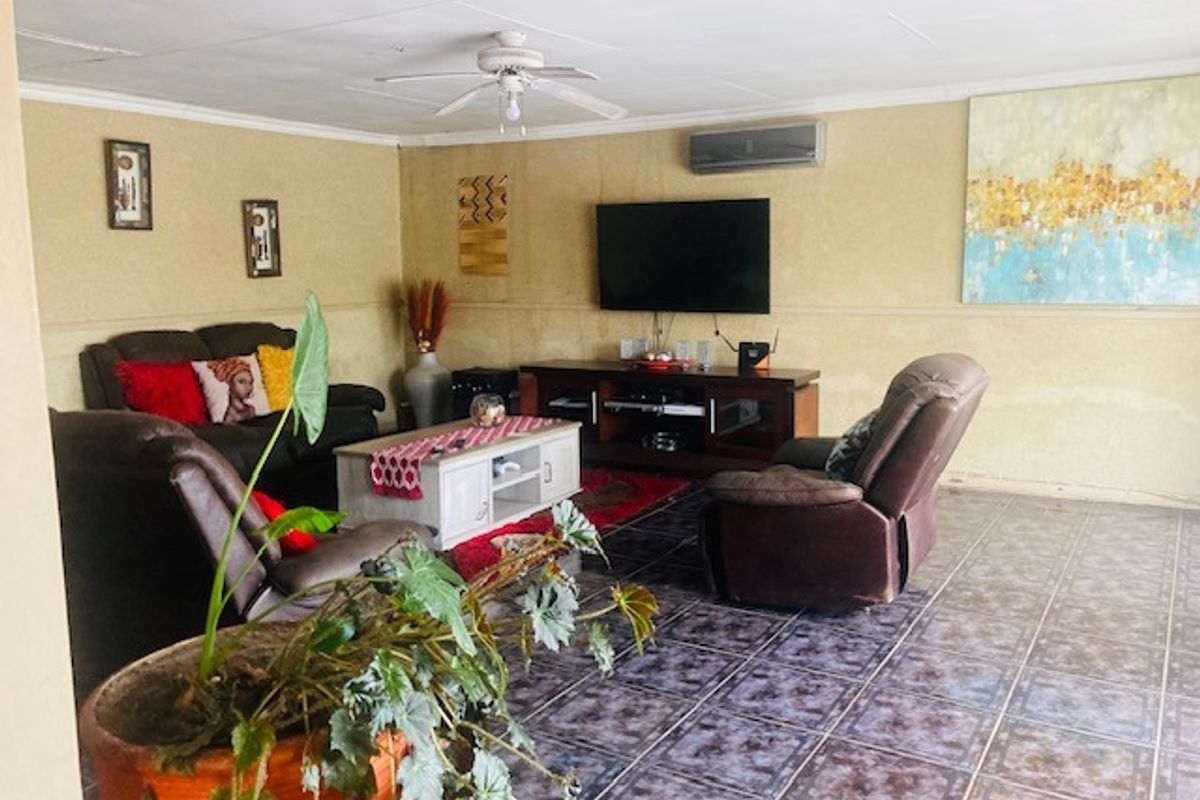Spacious living room featuring tiled flooring, a ceiling fan, and a wall-mounted air conditioning unit.