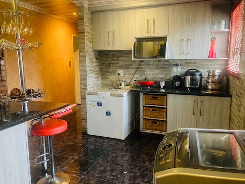 A functional kitchen featuring light wood-grain cabinetry, granite countertops, a tiled backsplash, and tiled flooring with an integrated microwave.