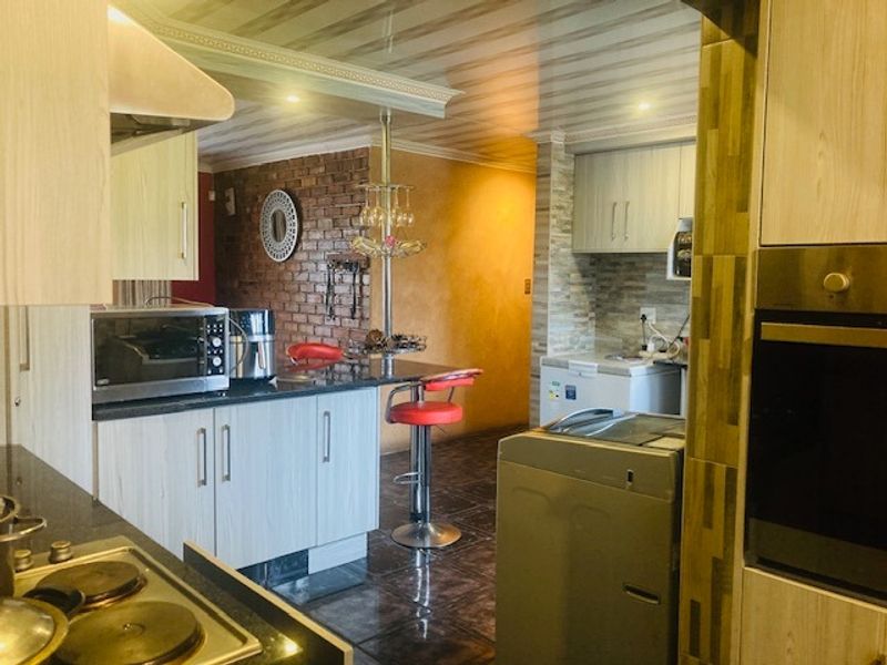 A functional kitchen featuring built-in cabinetry, granite countertops, an electric hob, and an integrated oven, with an adjacent breakfast bar and exposed brick wall.