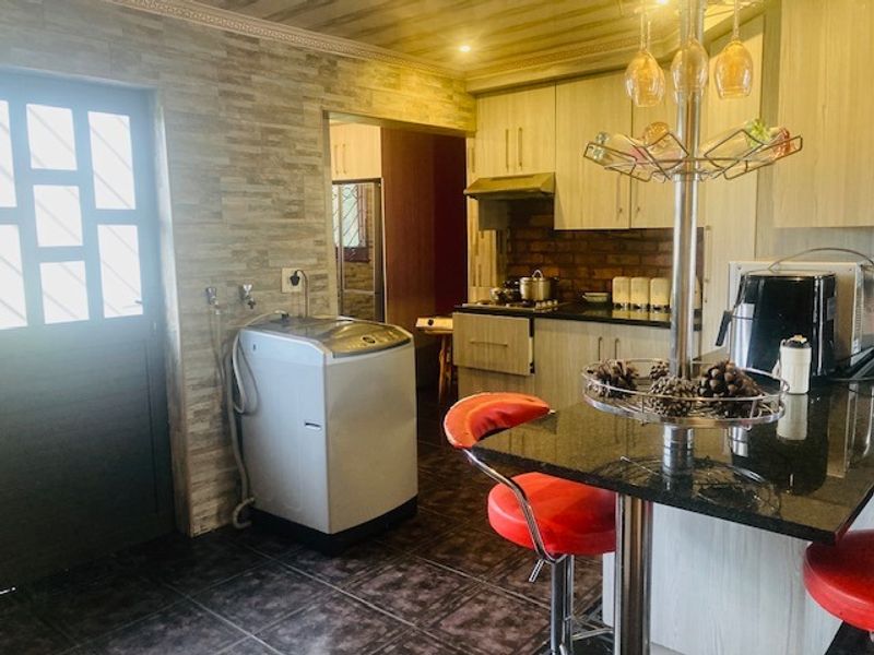 A functional kitchen featuring built-in cabinetry, granite countertops, a gas hob with extractor, and a stone-cladding feature wall with an integrated laundry area.