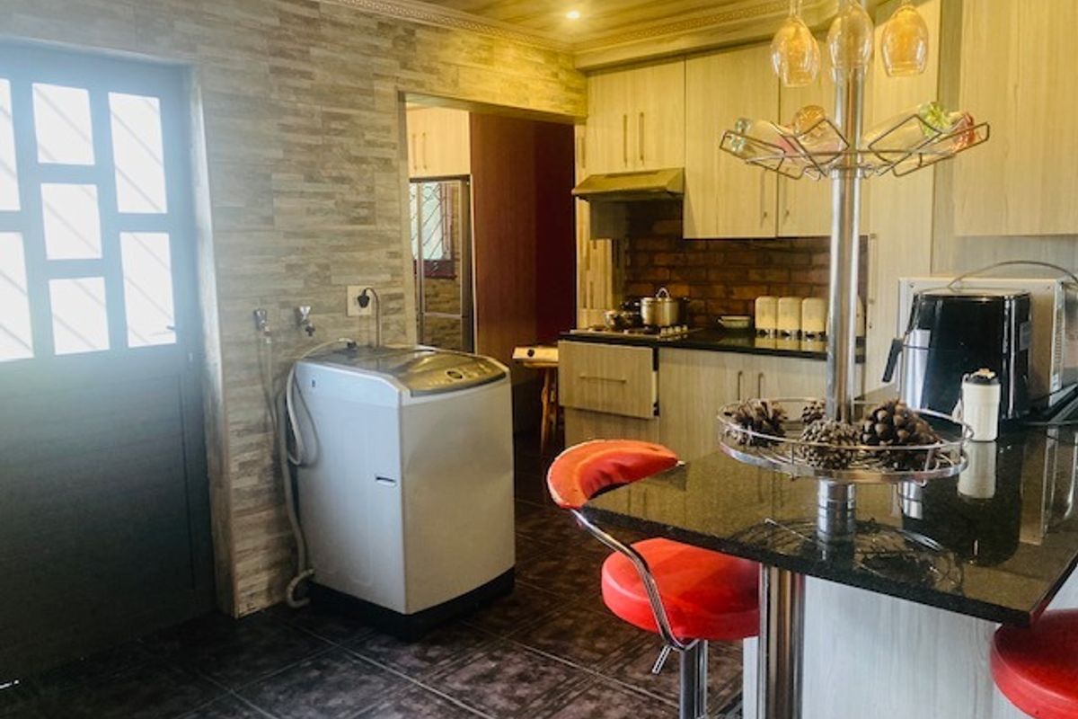 A functional kitchen featuring built-in cabinetry, granite countertops, a gas hob with extractor, and a stone-cladding feature wall with an integrated laundry area.