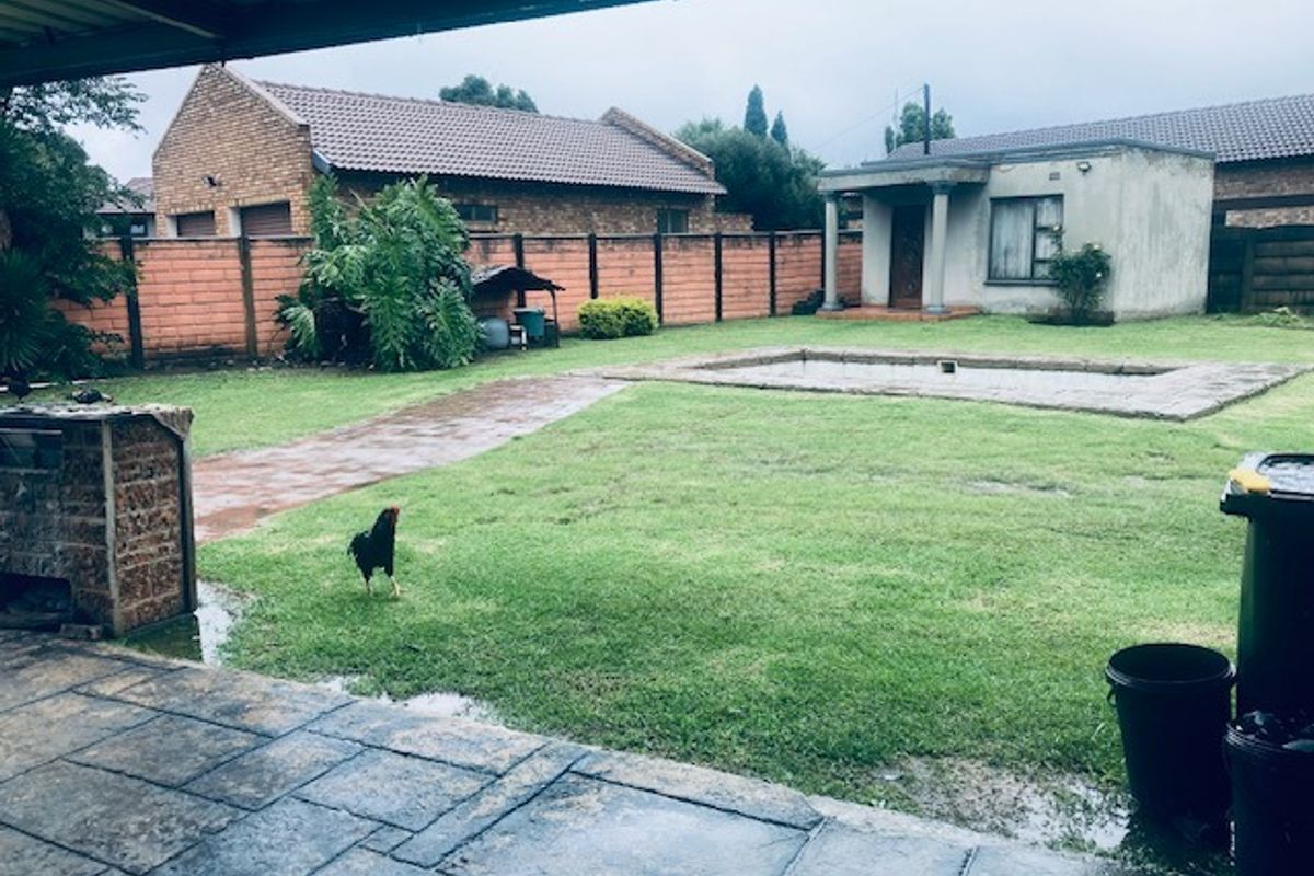 Spacious rear garden featuring a swimming pool, paved patio area, and brick boundary walls, viewed from a covered veranda.