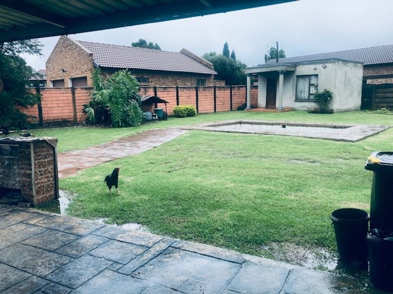 Spacious rear garden featuring a swimming pool, paved patio area, and brick boundary walls, viewed from a covered veranda.