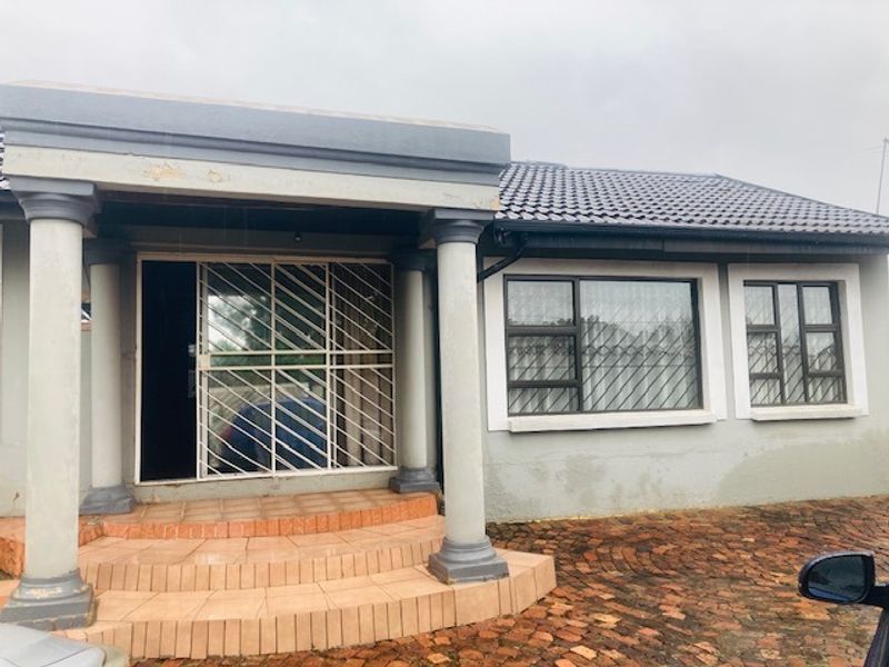 Front elevation of a single-story house featuring a tiled porch with concrete columns, security gates, and aluminium window frames with security bars.