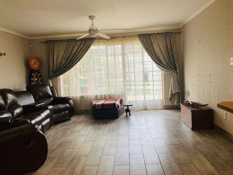 Spacious living room featuring tiled flooring, a ceiling fan, and large sliding glass doors that provide ample natural light.