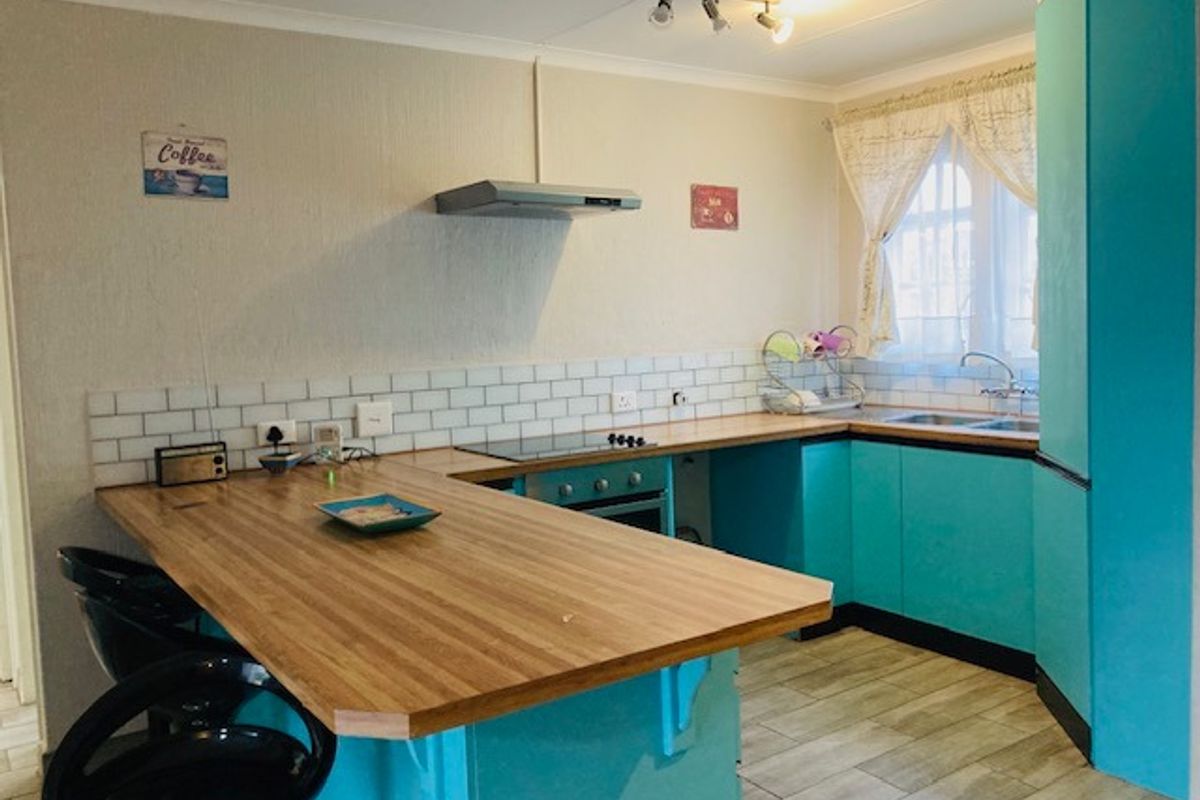 A functional kitchen featuring vibrant blue cabinetry, wood-look laminate countertops, a subway tile backsplash, and integrated cooking appliances.