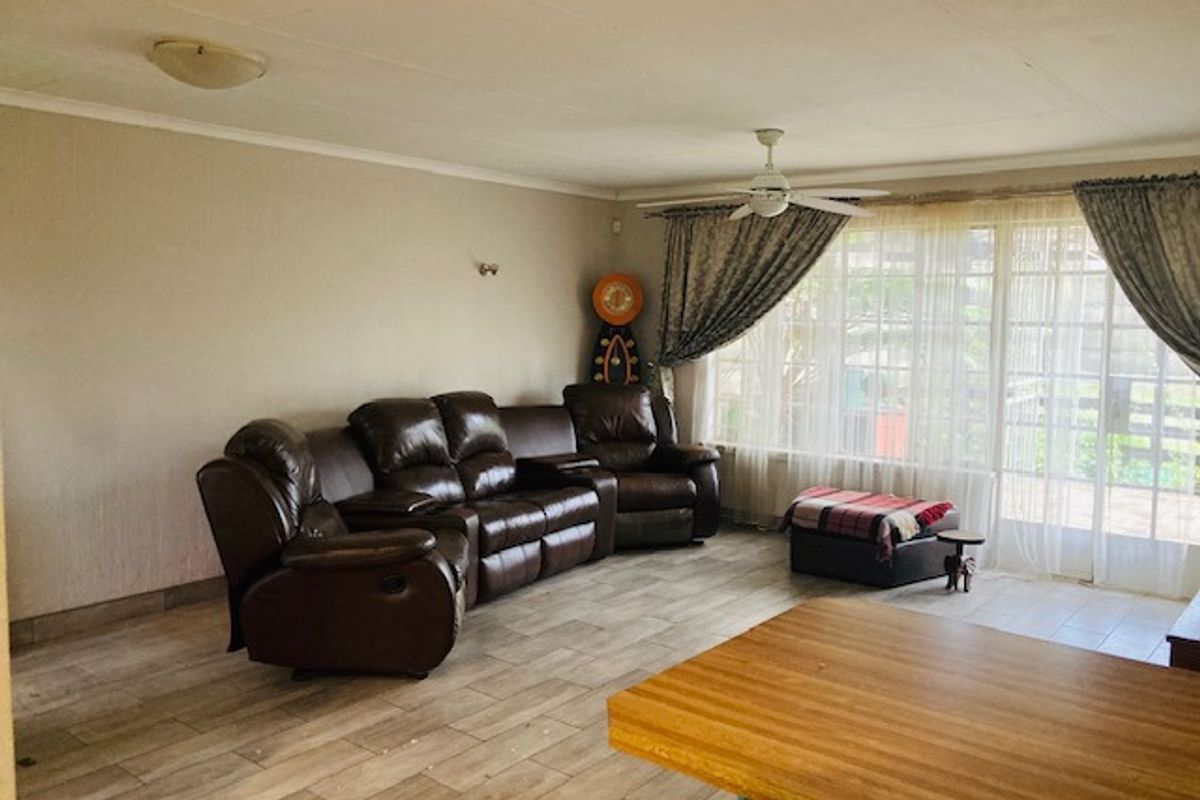 A spacious living room featuring tiled flooring, a ceiling fan, and large sliding glass doors that provide natural light and access to the outdoors.