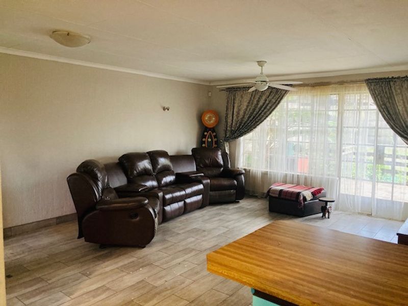 A spacious living room featuring tiled flooring, a ceiling fan, and large sliding glass doors that provide natural light and access to the outdoors.