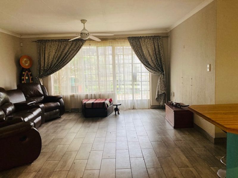 A spacious living room featuring tiled flooring, a ceiling fan, and large sliding glass doors that provide access to the exterior.
