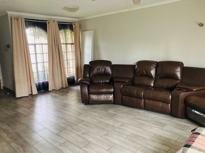 A spacious living room featuring light-toned tiled flooring, arched windows with natural light, and a ceiling fan.