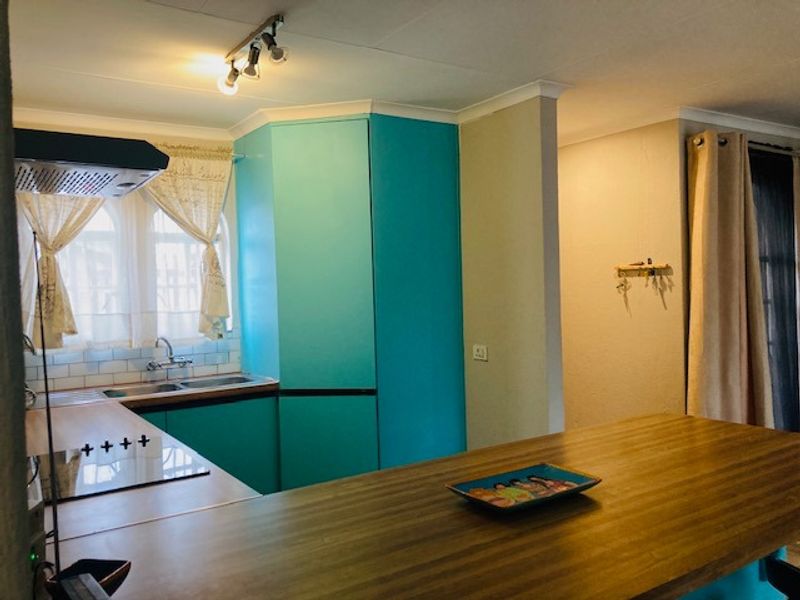 A kitchen featuring vibrant turquoise cabinetry, a built-in hob with extractor fan, and a functional sink area with tiled backsplash.