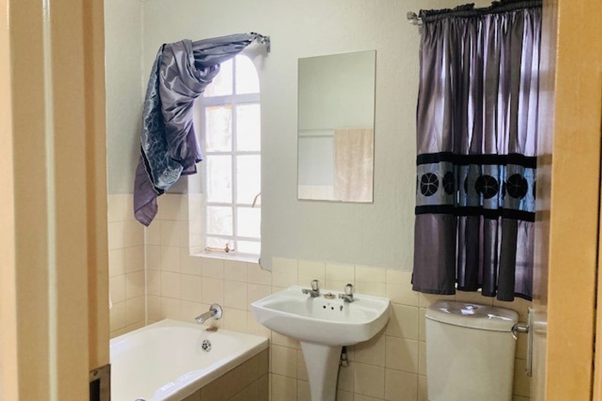 A functional bathroom featuring a pedestal washbasin, bathtub, and toilet with neutral wall finishes and tiled splashbacks.