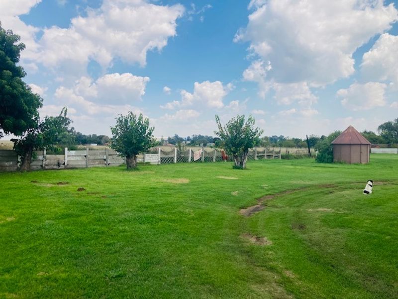 A spacious, open garden area featuring a perimeter wooden fence and a small circular outbuilding set against a rural landscape.