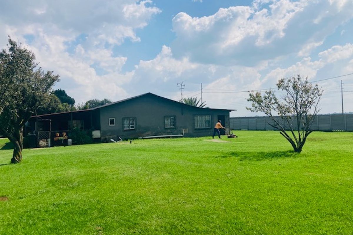 Rear view of the property featuring a large grass lawn, perimeter wall, and a covered patio area.