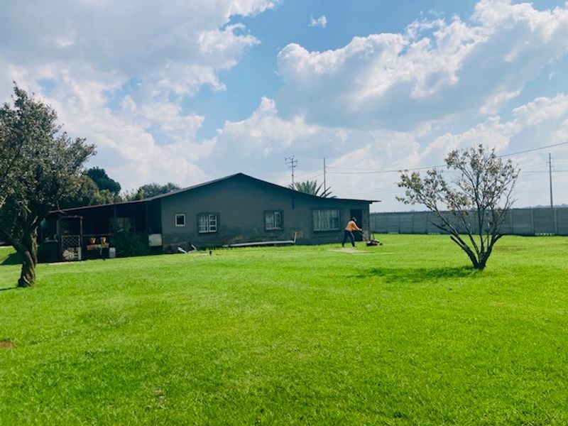 Rear view of the property featuring a large grass lawn, perimeter wall, and a covered patio area.