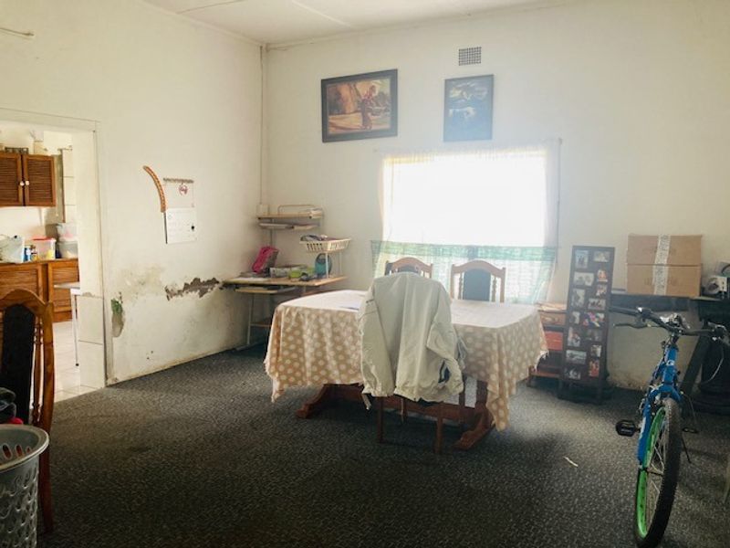 A living area featuring carpet flooring and a window, showing visible signs of wall plaster damage and wear requiring maintenance.