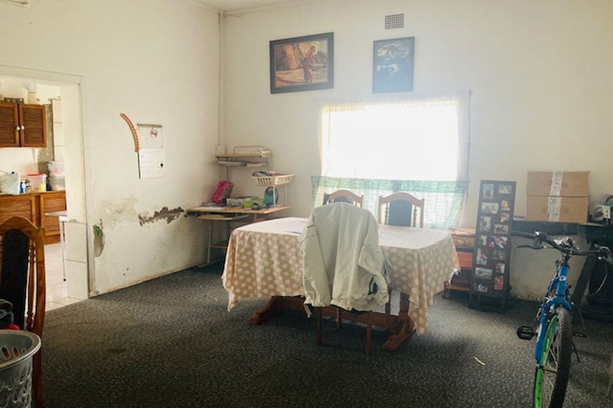 A living area featuring carpet flooring and a window, showing visible signs of wall plaster damage and wear requiring maintenance.