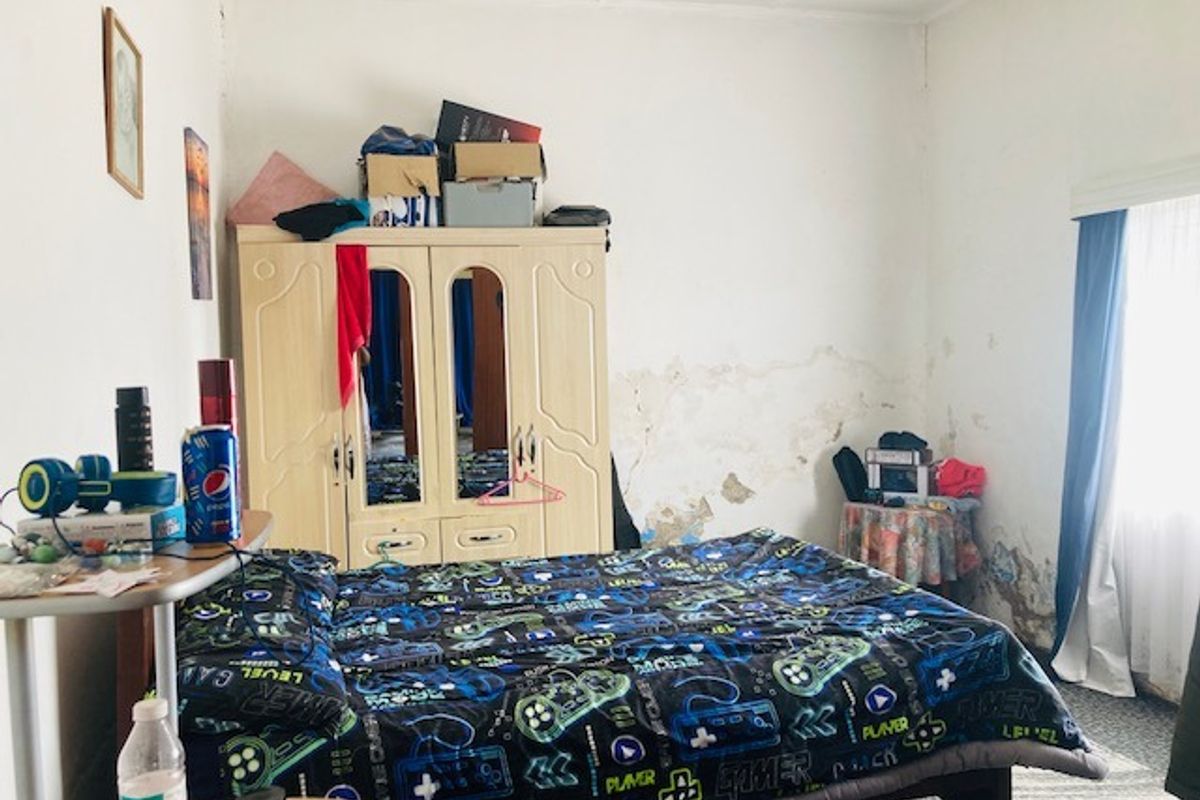 A bedroom featuring a window and significant wall surface damage requiring repair and redecoration.