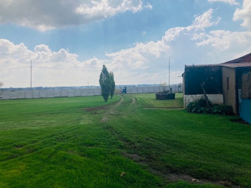 Expansive garden area featuring a large lawn, precast concrete boundary wall, and a dirt driveway track leading toward the property entrance.